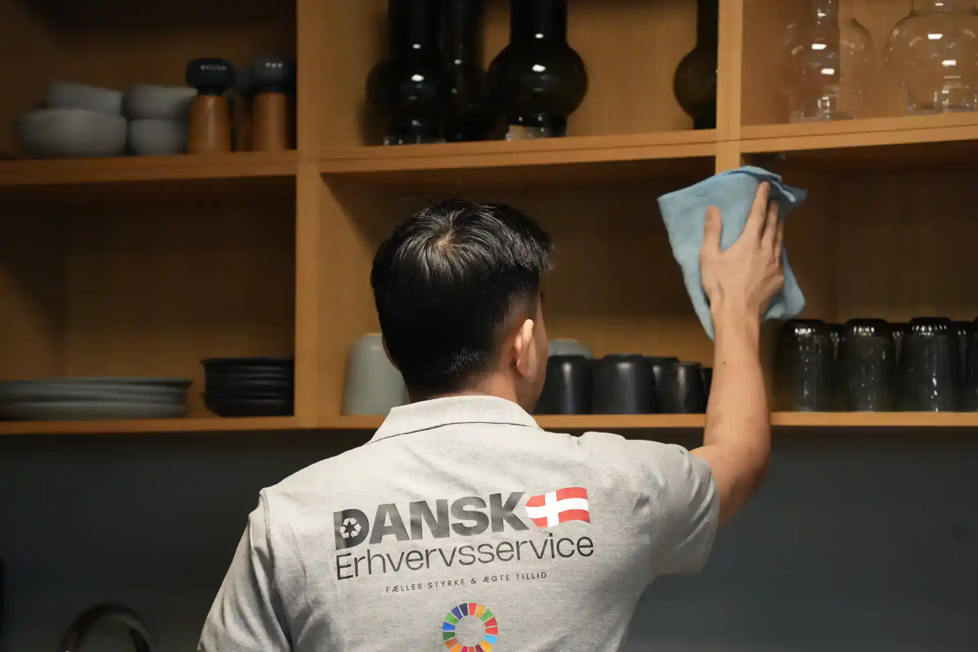 Rengøring af køkkenskabe med en person, der bruger en klud til at tørre hylder.