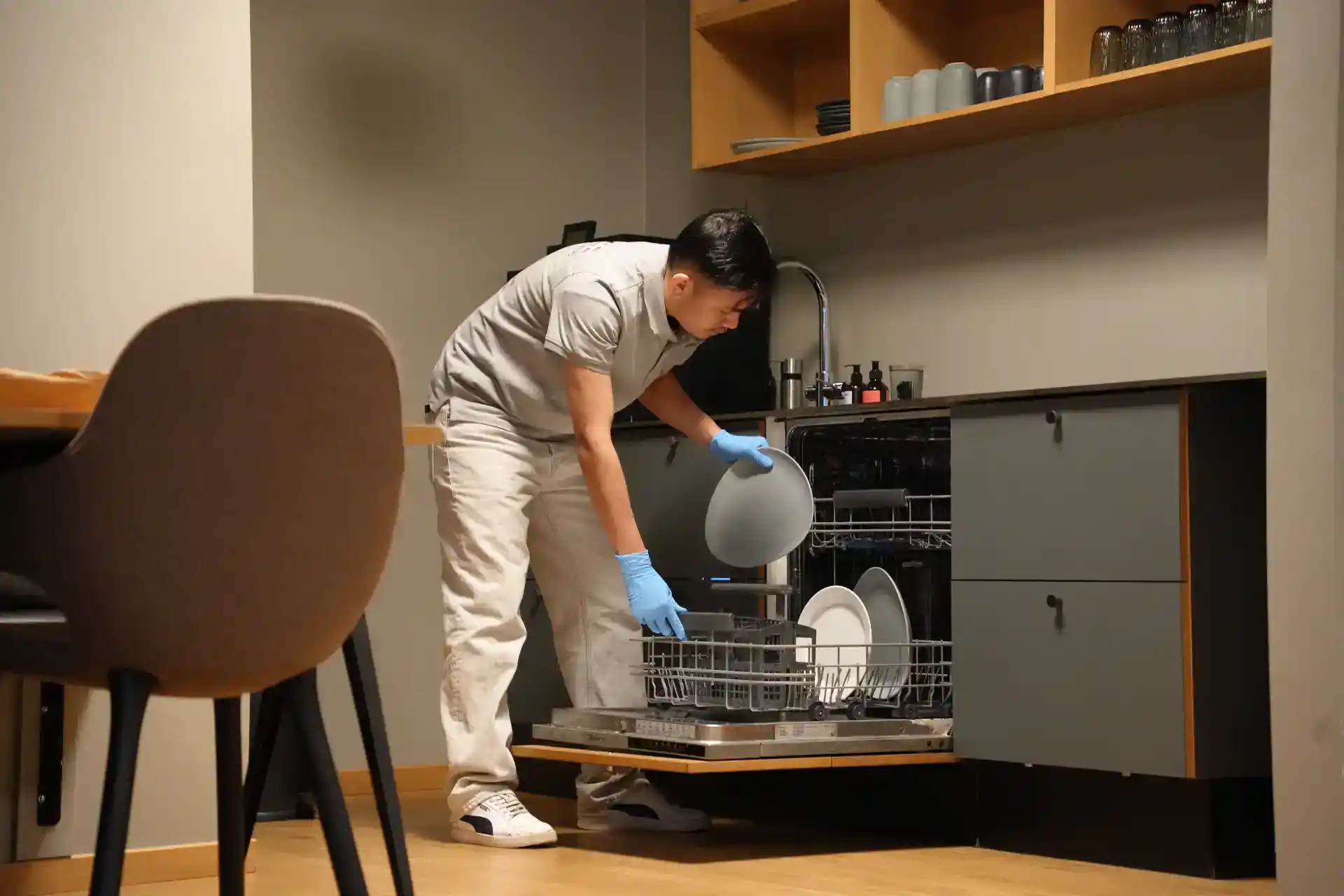 Rengøring af køkken med opvaskemaskine, person i handsker, klar til at vaske tallerkener.