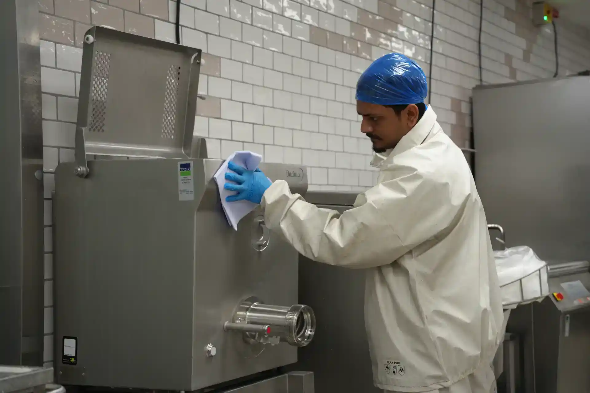 Mand i beskyttelsesudstyr arbejder med fødevareudstyr i et industrielt køkken.