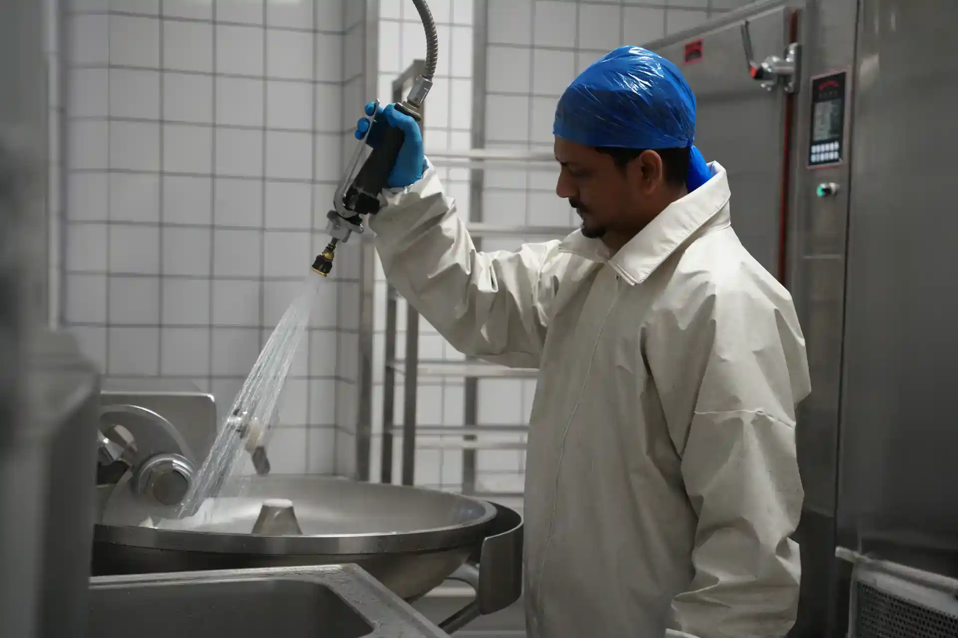 Mand i beskyttelsesudstyr vasker udstyr i fødevarefremstilling.