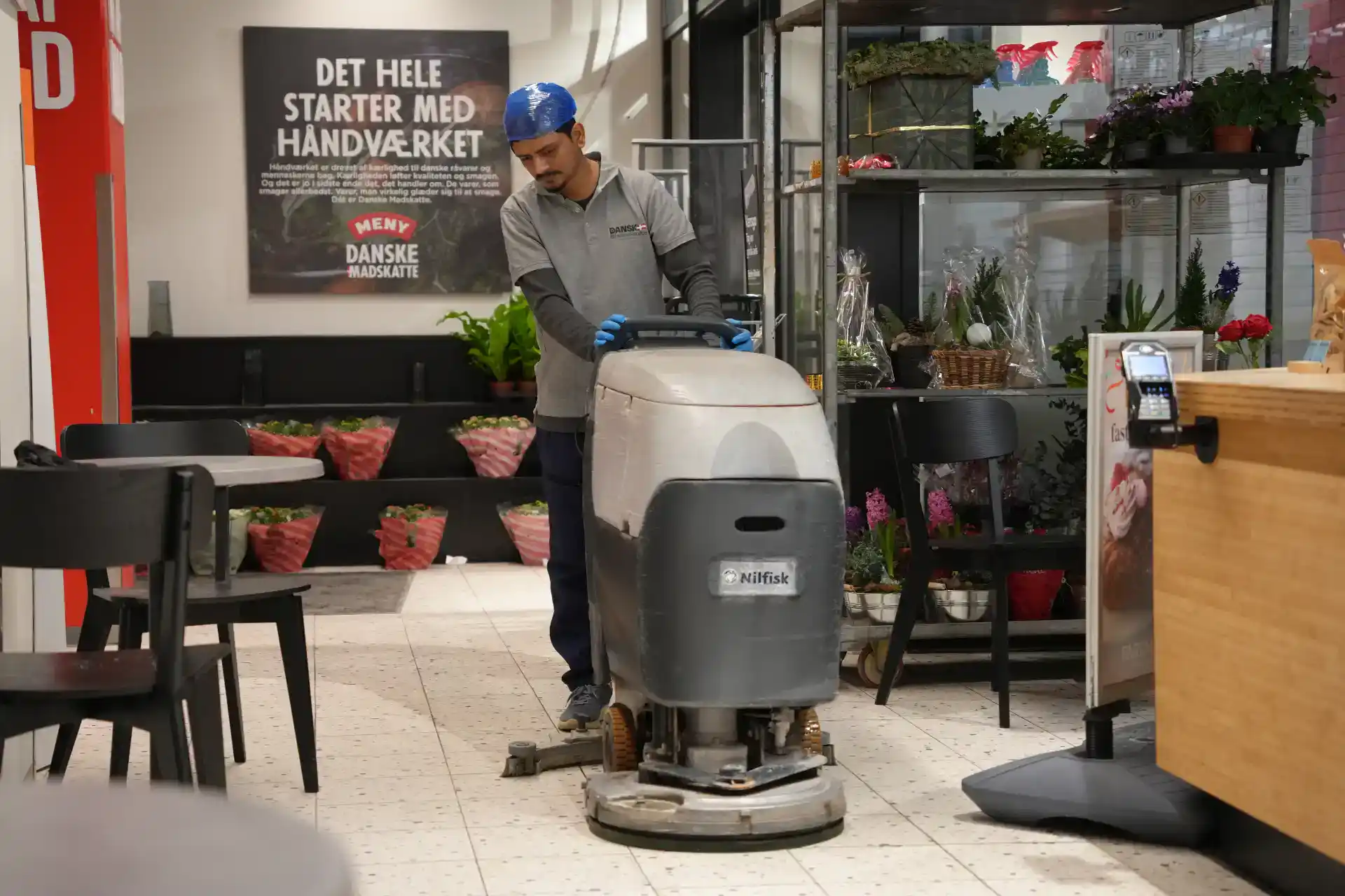 Rengøringsmedarbejder med gulvvaskemaskine i butiksmiljø.