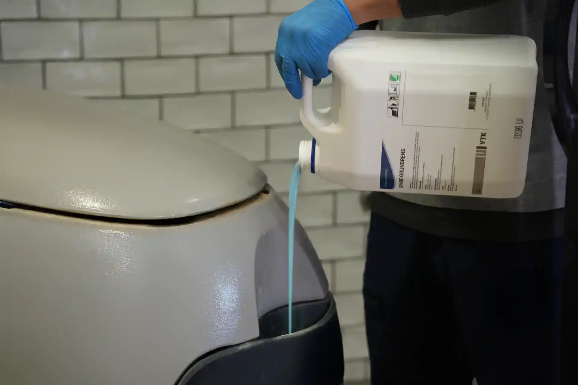 Person bruger kemikalier til vaskemaskine rengøring, iført blå handsker.