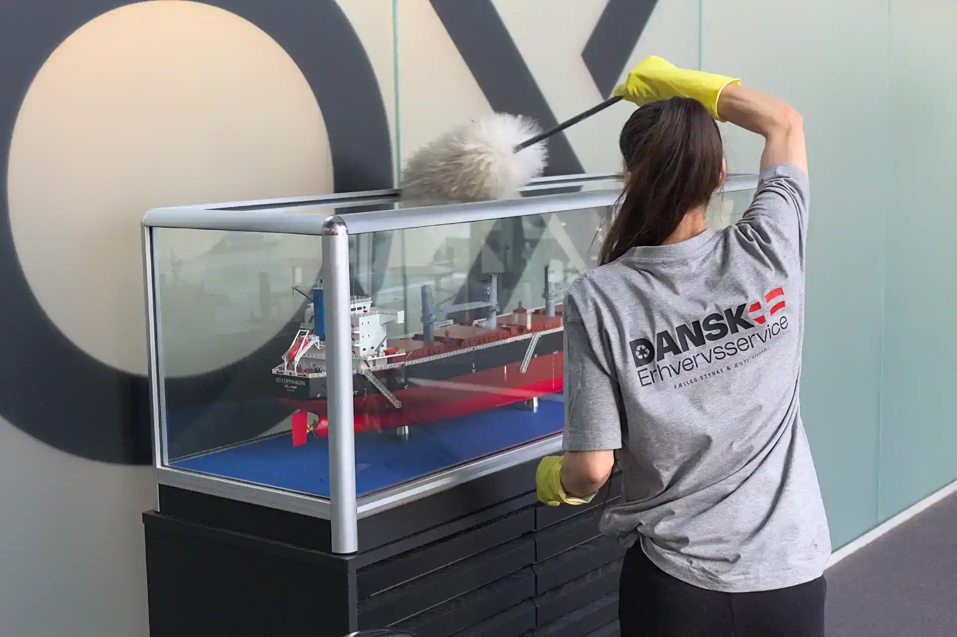 Kvinde med logo "Dansk Erhvervsservice" inspicerer modelskib i udstilling.