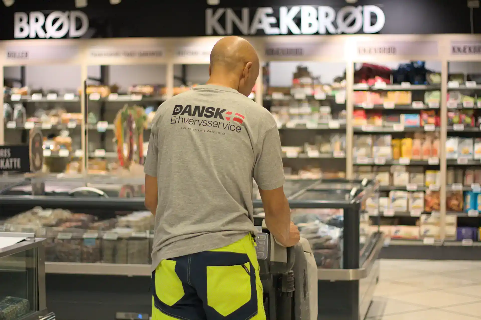 Butiksassistent i supermarked med Dansk Erhvervsservice logo på ryggen.