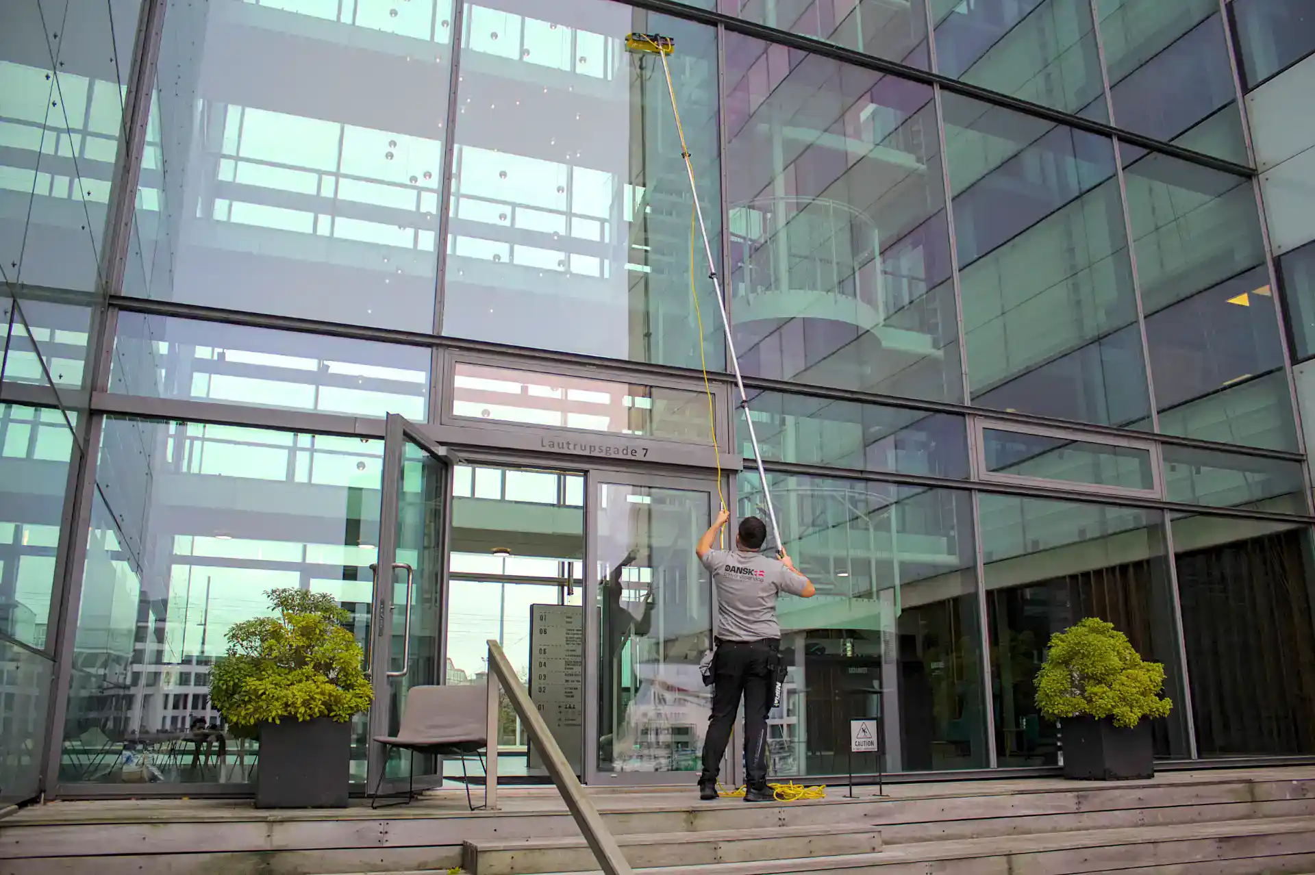 Rengøringsperson i uniform vasker vinduer på kontorbygning.