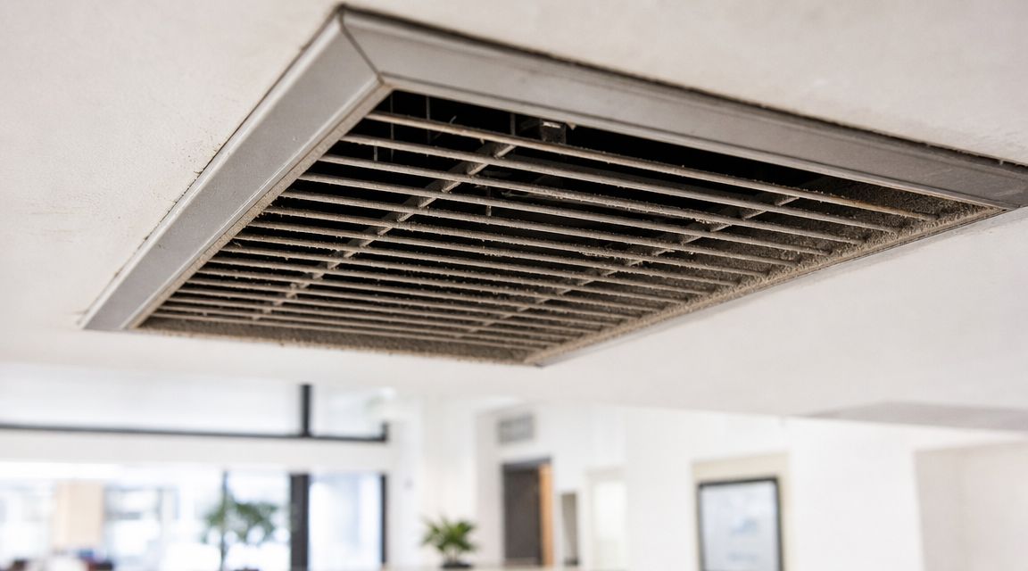 En beskidt og støvet ventilationsrist i loftet, der trænger til en grundig rengøring af ventilationsanlæg.
