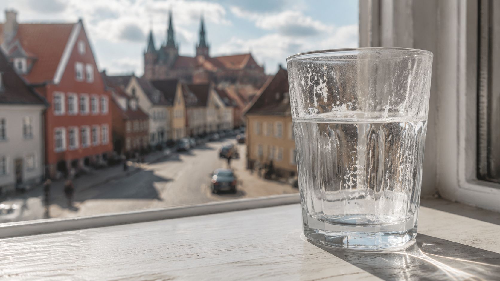 Et glas vand placeret på en vindueskarm med en flot udsigt over de historiske bygninger i Roskilde.